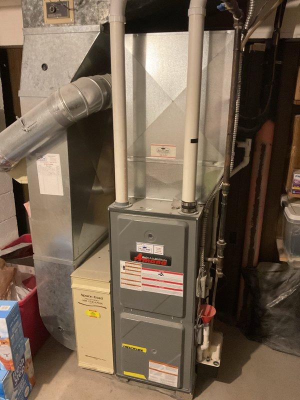 Provided comprehensive estimate for complete HVAC system replacement including outdoor air conditioning condenser unit and indoor furnace system. Assessed existing equipment configuration in basement utility area, documenting current gray metal furnace with vertical PVC venting, air handler with metallic ductwork, and outdoor white cabinet AC unit with top-discharge fan positioned on concrete pad adjacent to residence with electrical disconnect properly installed.