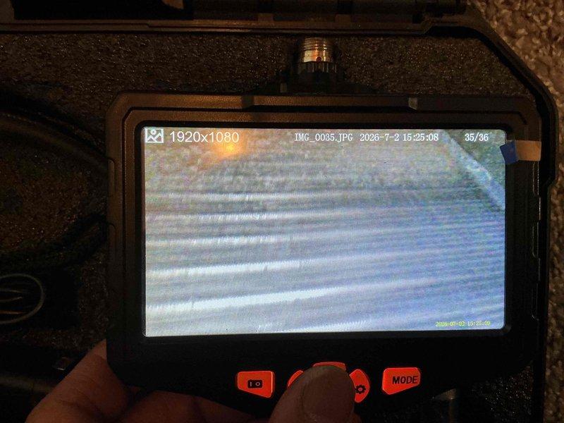Performed seasonal maintenance inspection on 19-year-old air conditioning system as part of an annual tune-up special. Upon arrival, found outdoor condensing unit in severely deteriorated condition with exterior panels missing and condenser coils heavily clogged with dirt, debris, and dried mud accumulation. Conducted thorough visual inspection of exposed internal components and utilized borescope camera to assess coil condition and verify extent of blockage throughout the heat exchanger fins. Unit's compromised state with missing protective housing and significant debris buildup was documented photographically for service records.