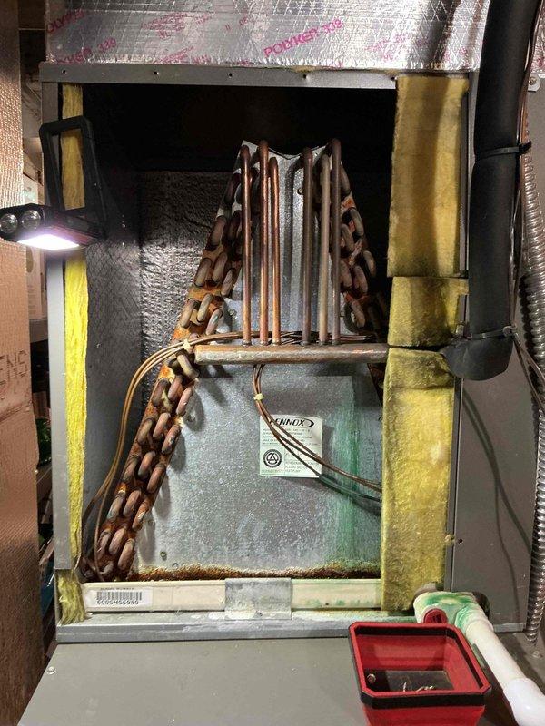 Completed annual air conditioning tune-up on 20-year-old Lennox system. Inspected evaporator coil assembly, verified refrigerant line connections, and documented condition of unit showing age-appropriate wear with minor oxidation on copper lines and rust staining on plenum housing. System operational and ready for cooling season.