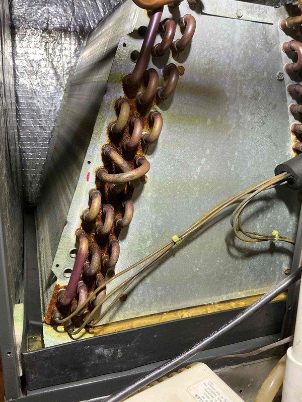 Completed scheduled cooling maintenance on a 5-year-old air conditioning system. Inspection revealed significant corrosion and oxidation on the evaporator coil's copper tubing, with rust-colored deposits visible on multiple U-bend connections and heavy deterioration on lower tube sections. The heat exchanger assembly showed advanced weathering with discoloration ranging from pink to dark brown, indicating prolonged exposure to moisture and potential efficiency loss. External components displayed substantial rust on the chain mechanism and metal housing panels, with visible staining and surface degradation. Documented all findings with photographs for maintenance records. System requires monitoring for refrigerant leaks and potential coil replacement in the near future due to the extent of corrosion observed.