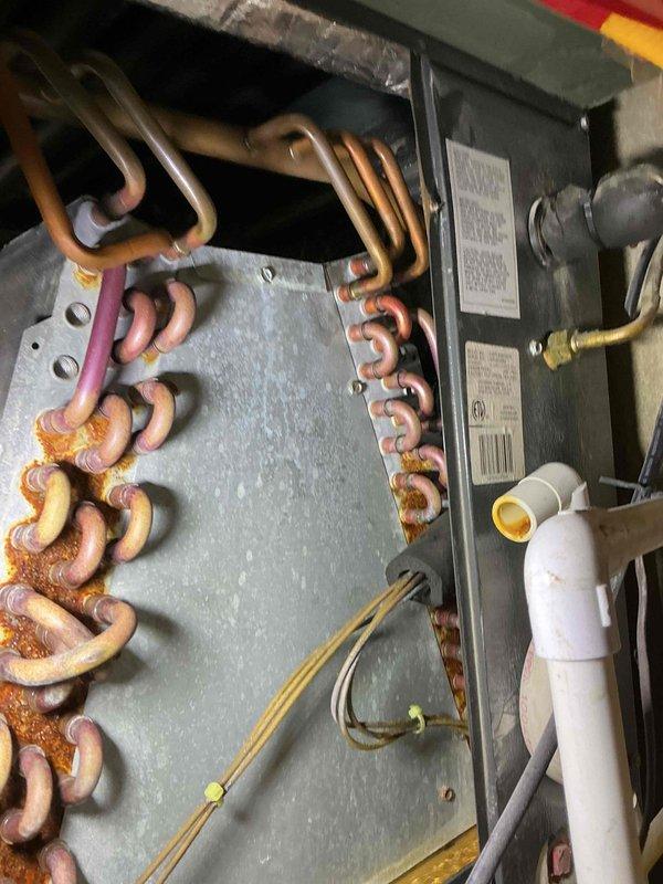 Completed scheduled cooling maintenance on a 5-year-old air conditioning system. Inspection revealed significant corrosion and oxidation on the evaporator coil's copper tubing, with rust-colored deposits visible on multiple U-bend connections and heavy deterioration on lower tube sections. The heat exchanger assembly showed advanced weathering with discoloration ranging from pink to dark brown, indicating prolonged exposure to moisture and potential efficiency loss. External components displayed substantial rust on the chain mechanism and metal housing panels, with visible staining and surface degradation. Documented all findings with photographs for maintenance records. System requires monitoring for refrigerant leaks and potential coil replacement in the near future due to the extent of corrosion observed.