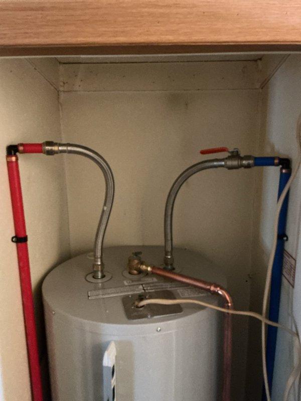Completed installation of a 50-gallon Bradford White electric water heater in an under-counter cabinet space. Connected hot and cold water supply lines using flexible braided stainless steel connectors with shut-off valves, installed temperature and pressure relief valve with discharge piping, and verified all plumbing connections for proper operation and leak-free performance.