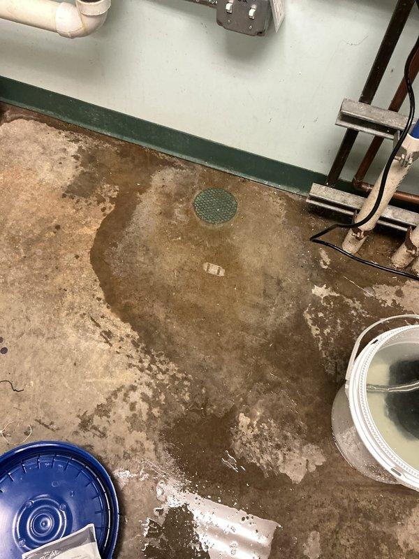 Responded to service call for water on floor beneath air conditioning system. Upon arrival, found significant water accumulation on concrete basement floor around HVAC equipment area. Inspected condensate drain system and backflow preventer assembly. Identified clogged condensate drain line as source of water overflow. Cleared blockage from drain line, verified proper drainage flow, and confirmed backflow device operational. Cleaned up standing water and monitored system to ensure proper condensate evacuation restored.