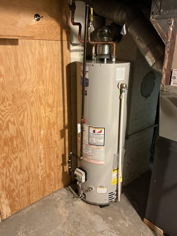 Replaced aging 40-gallon natural gas water heater in basement utility room of residential property built in 1928. Removed deteriorated existing unit showing significant corrosion and exterior degradation, then installed new white tank water heater with proper copper piping connections, temperature and pressure relief valve, and code-compliant venting. All plumbing connections secured with appropriate fittings, gas line reconnected, and unit tested for proper operation and safety compliance.