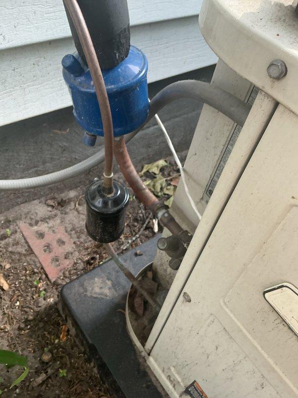 # No Cool Service Call

Responded to a no cooling complaint on a residential air conditioning system. Upon arrival, performed system diagnostics and visual inspection of outdoor condensing unit. Unit identified as Goodman model 5504MX024000PAAP with serial number U488990432. 

Inspected refrigerant lines, filter drier, and compressor connections at outdoor unit. Observed typical wear and environmental exposure on equipment exterior with accumulated dirt and debris on components and surrounding concrete pad. Verified proper electrical connections and examined refrigerant line routing along building exterior. System components including blue filter drier and copper refrigerant lines inspected for leaks, damage, or restrictions.

Documented equipment condition with photographs showing nameplate data, piping configuration, and component layout. Unit factory charged with refrigerant per specifications on data plate showing piston ID 63 and OD 117.8 measurements. All findings and system info