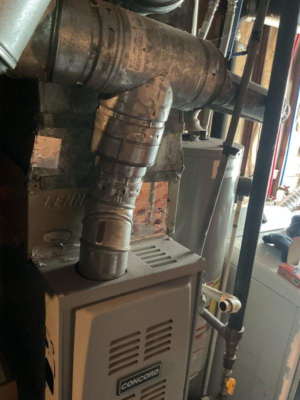 Completed estimate for adding air conditioning system to existing Concord furnace installation in residential garage utility space. Assessed current heating equipment, evaluated heavily corroded ductwork system showing significant rust and oxidation on elbow joints and vertical sections, and documented existing furnace configuration with adjacent water heater. Provided recommendations for AC unit integration, necessary ductwork repairs or replacement due to advanced deterioration, and proper system sizing to match existing furnace capacity for optimal cooling performance.