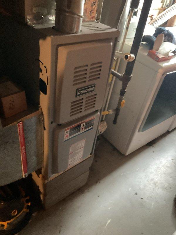 Completed estimate for adding air conditioning system to existing Concord furnace installation in residential garage utility space. Assessed current heating equipment, evaluated heavily corroded ductwork system showing significant rust and oxidation on elbow joints and vertical sections, and documented existing furnace configuration with adjacent water heater. Provided recommendations for AC unit integration, necessary ductwork repairs or replacement due to advanced deterioration, and proper system sizing to match existing furnace capacity for optimal cooling performance.