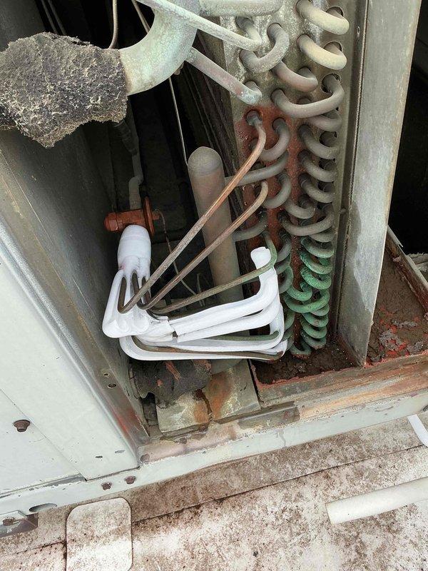 # Commercial Rooftop AC Unit - No Cooling Complaint

Responded to no cooling complaint on commercial rooftop air conditioning unit. Upon arrival, accessed unit via side entrance as instructed and proceeded to rooftop for diagnostic evaluation.

## Inspection Findings

Conducted thorough visual inspection of rooftop unit interior components. Found evaporator coil exhibiting severe corrosion and oxidation throughout its serpentine structure. Coil displayed progressive deterioration with white oxidation on upper sections, rust-colored corrosion in middle portions, and green-blue copper patina on lower coils, indicating prolonged moisture exposure and chemical degradation.

Observed substantial dirt and debris accumulation throughout unit cabinet, particularly at base and on mechanical components. Blower assembly showed heavy dust and lint buildup on motor and housing. Interior surfaces displayed rust staining and general deterioration consistent with extended service life in harsh environ