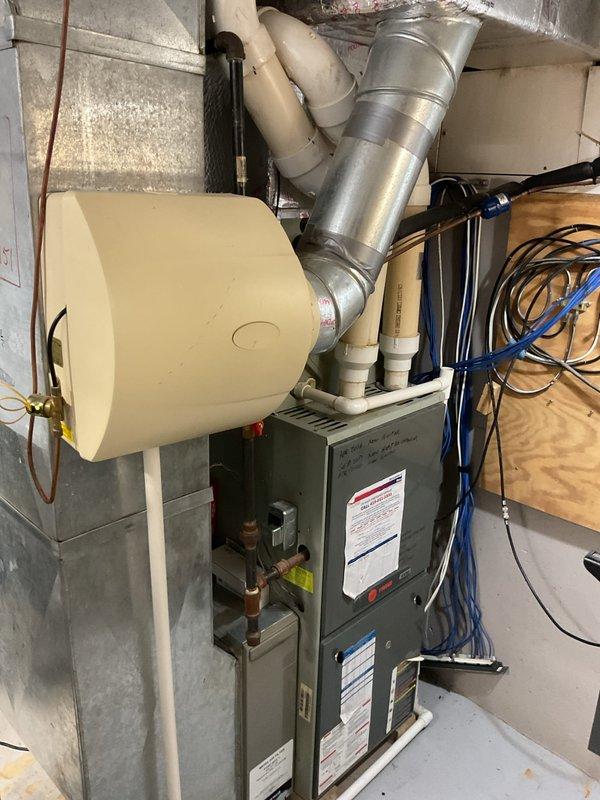 Completed comprehensive evaluation of existing HVAC system for full replacement estimate. Assessed current furnace unit, humidifier, and air conditioning components in basement mechanical room. Documented existing equipment configuration including gray metal furnace with attached cylindrical humidifier unit, metallic ductwork, PVC drainage piping, copper refrigerant lines, gas connections, and electrical wiring. Evaluated utility connections, venting requirements, and available space for new equipment installation. Captured detailed photographs of current system layout to provide accurate replacement recommendations and ensure proper sizing for new furnace and AC units.