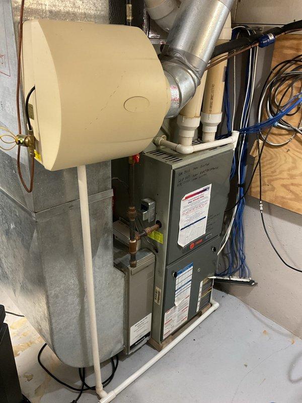 Completed comprehensive evaluation of existing HVAC system for full replacement estimate. Assessed current furnace unit, humidifier, and air conditioning components in basement mechanical room. Documented existing equipment configuration including gray metal furnace with attached cylindrical humidifier unit, metallic ductwork, PVC drainage piping, copper refrigerant lines, gas connections, and electrical wiring. Evaluated utility connections, venting requirements, and available space for new equipment installation. Captured detailed photographs of current system layout to provide accurate replacement recommendations and ensure proper sizing for new furnace and AC units.