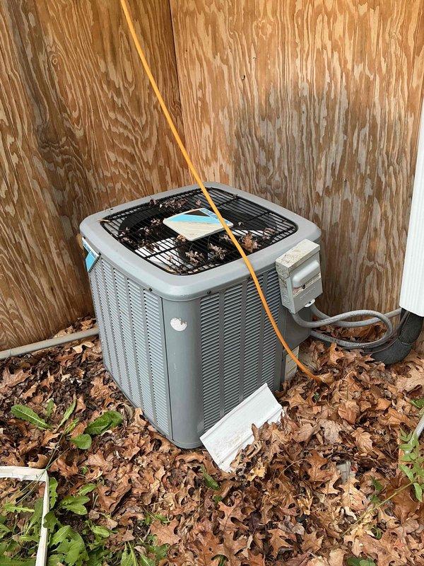 # HVAC Service Call - No Cooling Issue

Responded to service call for 10-year-old residential air conditioning system that failed to turn on. Upon arrival, performed visual inspection of outdoor condenser unit located against exterior building wall. Unit showed signs of neglect with significant leaf litter and organic debris accumulation around base and heavy vegetation growth obstructing airflow to lower intake areas.

Verified electrical disconnect box present at unit location. Traced copper refrigerant lines and electrical conduit connections from unit to building. Checked power supply at disconnect and confirmed electrical connection integrity. Cleared debris field surrounding condenser unit to restore proper airflow clearance and prevent future operational issues.

Performed system startup sequence and verified compressor engagement. Tested contactor operation and confirmed proper voltage delivery to unit components. System restored to operational status with cooling functionality