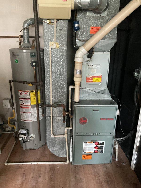 Conducted comprehensive assessment of existing HVAC system and water heating equipment for replacement estimate. Evaluated exterior air conditioning unit showing significant age and weathering, noting older-style condenser with deteriorated cabinet finish and outdated components positioned on concrete pad adjacent to residential structure. Documented existing electrical service configuration including meter location and conduit routing for proper system sizing and electrical requirements.

Inspected interior equipment including existing Rheem furnace and cylindrical water heater in utility area. Assessed current venting configuration with PVC exhaust system, existing ductwork connections, and plumbing infrastructure including copper supply lines, pressure relief valves, and gas piping. Evaluated space constraints and equipment access for replacement installation planning. Documented all utility connections, clearances, and structural considerations necessary for accurate equipment spec