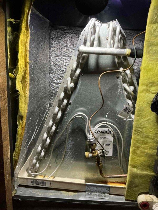 Completed preventative maintenance on 13-year-old air conditioning system. Inspected evaporator coil assembly in attic installation, noting dust accumulation on aluminum fins and operational UV light system mounted to air handler for air quality enhancement. Replaced air filter as requested and verified proper condensate drainage through Lennox drain pan and trap assembly.