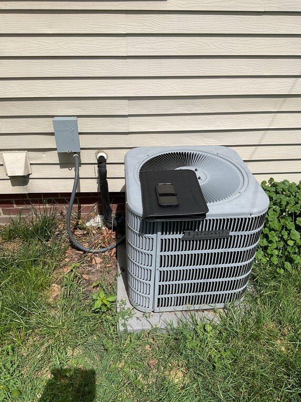 Performed comprehensive assessment of existing HVAC system for complete air conditioning replacement. Evaluated outdoor condenser unit with cylindrical design and black horizontal grille fins currently positioned on grass adjacent to building exterior. Documented existing electrical disconnect box and utility connections, including conduit routing from building-mounted components to ground-level equipment. Assessed indoor components including water heater and associated plumbing infrastructure in basement utility area to ensure compatibility with proposed AC system replacement and verify adequate clearances for new equipment installation.