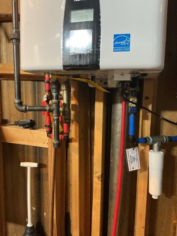 Completed professional installation of a wall-mounted Navien tankless water heater in utility area with exposed stud framing. Mounted unit securely to wall structure and established all necessary connections including hot and cold water supply lines with color-coded piping (red for hot, blue for cold), PVC venting system routed through top of unit, gas supply line with appropriate shut-off valves, and electrical connections via flexible metal conduit. Installed isolation valves on both water supply lines for future maintenance access and incorporated sediment filter on cold water inlet to protect unit from debris. Completed all venting requirements per manufacturer specifications using white PVC pipe. Verified proper operation of digital control panel and tested unit for leaks at all connection points. Installation meets current plumbing codes and Energy Star efficiency standards.
