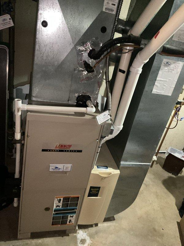 Completed comprehensive assessment of existing HVAC system for replacement estimate. Evaluated outdoor Lennox condenser unit with cylindrical design showing signs of age and weathering, surrounded by overgrown vegetation requiring clearance for proper airflow. Documented indoor Lennox furnace installation in basement mechanical room, including existing ductwork configuration, plenum connections, PVC condensate drainage system, and electrical service requirements. Photographed current system specifications and equipment labels to provide accurate replacement recommendations and ensure proper sizing for new equipment installation.