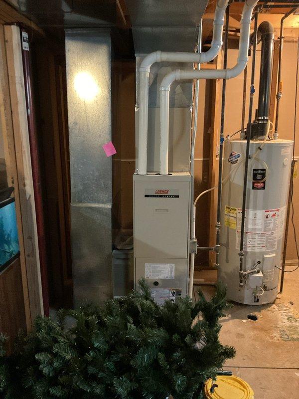 Conducted comprehensive assessment of existing HVAC system for complete replacement estimate. Evaluated outdoor condensing unit positioned on concrete pad with electrical disconnect, noting weathered condition and vegetation encroachment affecting clearances. Inspected basement furnace installation including Lennox gas furnace with overhead ductwork configuration and adjacent water heater. Documented current equipment specifications, electrical connections, duct routing, and installation conditions to provide accurate replacement recommendations for both heating and cooling systems.
