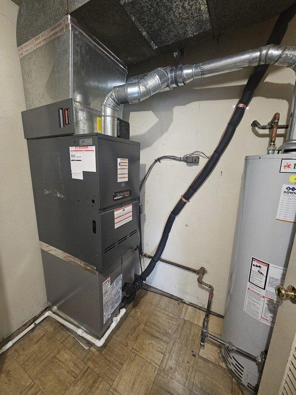 Completed installation of downflow air conditioning system with evaporator coil package integrated with existing Lennox furnace unit in residential utility room. Installed new A/C coil assembly above furnace with proper ductwork connections, configured refrigerant line set with isolation valves, and mounted electrical control box on wall with active status indicator. Verified all mechanical connections, tested system operation, and ensured proper airflow through metallic ductwork transitions.