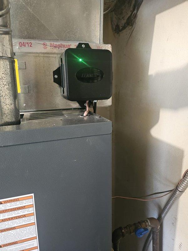 Completed installation of downflow air conditioning system with evaporator coil package integrated with existing Lennox furnace unit in residential utility room. Installed new A/C coil assembly above furnace with proper ductwork connections, configured refrigerant line set with isolation valves, and mounted electrical control box on wall with active status indicator. Verified all mechanical connections, tested system operation, and ensured proper airflow through metallic ductwork transitions.