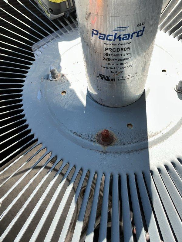 Completed preventative maintenance on air conditioning system over 10 years old. Inspected dual-run capacitor showing weathered condition with surface oxidation and rust present on mounting hardware; verified electrical specifications at 50+5 MFD 370VAC within acceptable parameters. Measured system amperage at 44.5 amps using clamp meter, confirming proper electrical operation. Cleaned condenser coil fins of accumulated dirt and debris, checked all electrical connections at control board, and verified proper wire terminations throughout unit.