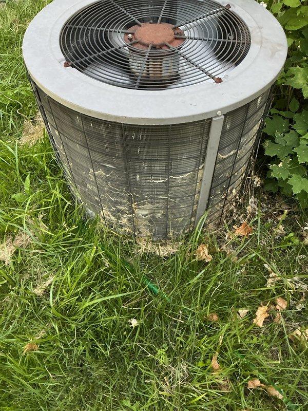 # HVAC Service Report

Responded to no-cooling complaint on residential air conditioning system. Upon arrival, found outdoor condenser unit in overgrown area with significant dirt and debris accumulation on protective grilles and fan assembly. Unit showed signs of extended outdoor exposure with weathering, discoloration, and grime buildup affecting airflow efficiency. Inspected fan motor assembly and noted corrosion on central hub mechanism. Cleared vegetation and debris from around unit perimeter to restore proper airflow clearance. Cleaned condenser coils and protective mesh screening to remove accumulated dirt and organic matter. Tested system operation and verified proper fan rotation and compressor function. Recommended ongoing vegetation management around unit and regular maintenance schedule to prevent future airflow restrictions.