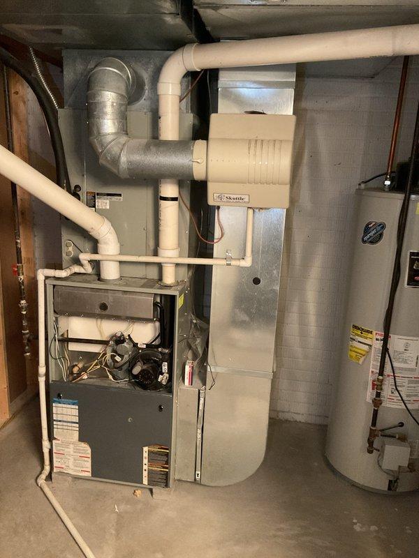 Completed comprehensive estimate for full HVAC system replacement at residential property. Assessed existing basement-mounted gas furnace with humidifier integration and outdoor condensing unit positioned on exterior concrete pad against home's foundation. Documented current equipment configuration including PVC venting system, ductwork connections, and electrical service routing. Photographed interior mechanical room showing furnace with exposed access panel, connected humidification system, and adjacent water heater for reference. Evaluated outdoor condenser unit condition, refrigerant line routing through exterior wall penetration, and electrical disconnect panel placement. Provided detailed replacement recommendations for complete heating and cooling system upgrade to meet current efficiency standards and homeowner comfort requirements.