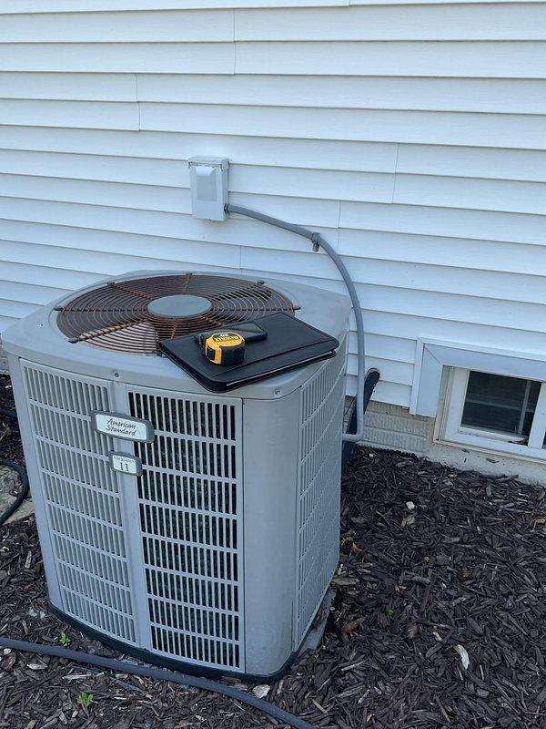 Completed comprehensive estimate for full HVAC system replacement at residential property. Assessed existing basement-mounted gas furnace with humidifier integration and outdoor condensing unit positioned on exterior concrete pad against home's foundation. Documented current equipment configuration including PVC venting system, ductwork connections, and electrical service routing. Photographed interior mechanical room showing furnace with exposed access panel, connected humidification system, and adjacent water heater for reference. Evaluated outdoor condenser unit condition, refrigerant line routing through exterior wall penetration, and electrical disconnect panel placement. Provided detailed replacement recommendations for complete heating and cooling system upgrade to meet current efficiency standards and homeowner comfort requirements.