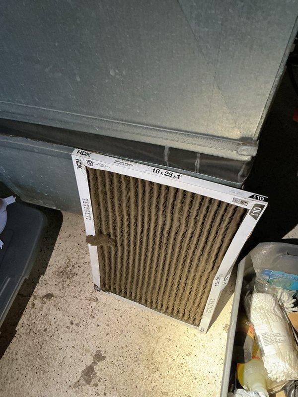 # HVAC Service Report - No Cooling Complaint

Responded to a no cooling complaint on a central air conditioning system over ten years old. Upon arrival, performed a complete system evaluation to diagnose the cooling failure.

Inspected the indoor air handler and discovered a severely restricted air filter with heavy dust and debris accumulation. The 16x25x1 filter media was completely saturated with brown and tan particulate matter, significantly impeding airflow through the system. This restriction was causing inadequate air circulation across the evaporator coil, preventing proper heat exchange and resulting in the no cooling condition.

Removed and replaced the heavily soiled air filter with a new unit. Examined the evaporator coil area and noted dust accumulation on internal components and housing, consistent with prolonged operation under restricted airflow conditions. Inspected refrigerant lines and connections for any signs of damage or leakage - copper refrigerant piping appear