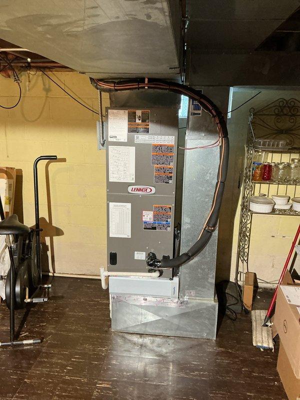 Completed full split system HVAC installation featuring a Lennox single-stage condenser unit positioned on a composite pad with white decorative rock landscaping against the brick exterior, and an upflow air handler installed in the basement utility area. Fabricated custom return base with 5-inch rack, ran new supply and return drops, installed 3/4-inch by 20-foot lineset with proper insulation, mounted electrical disconnect and whip, and added outdoor surge protection for equipment longevity. Ran dedicated electrical circuit to outdoor unit while tying into existing service, replaced thermostat for system control, and ensured all refrigerant lines, electrical conduit, and ductwork connections were properly secured and code-compliant.