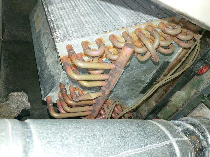 Returned to unit after defrost cycle completed to perform diagnostic evaluation. Upon inspection, found extensive corrosion and oxidation throughout copper refrigerant lines and evaporator coil assembly, indicating prolonged moisture exposure and age-related deterioration. Documented condition of heat exchanger components, insulated refrigerant lines, and internal HVAC system framework showing significant environmental wear and compromised integrity of metal surfaces.