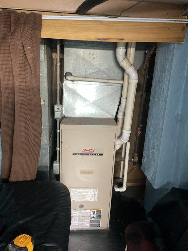 Conducted comprehensive assessment of existing HVAC system for complete replacement estimate. Evaluated outdoor condensing unit positioned on concrete pad adjacent to building exterior, noting beige unit with vertical louvers and top-mounted fan grille with protective covering in place. Inspected electrical disconnect box mounted to structure and associated conduit routing. Documented indoor equipment including Lennox furnace installation located in basement utility area between floor joists. Assessed existing white PVC venting configuration, silver ductwork installation, and overall mechanical space layout. Photographed both outdoor and indoor components to document current system condition and facilitate accurate equipment sizing and replacement specifications for estimate preparation.