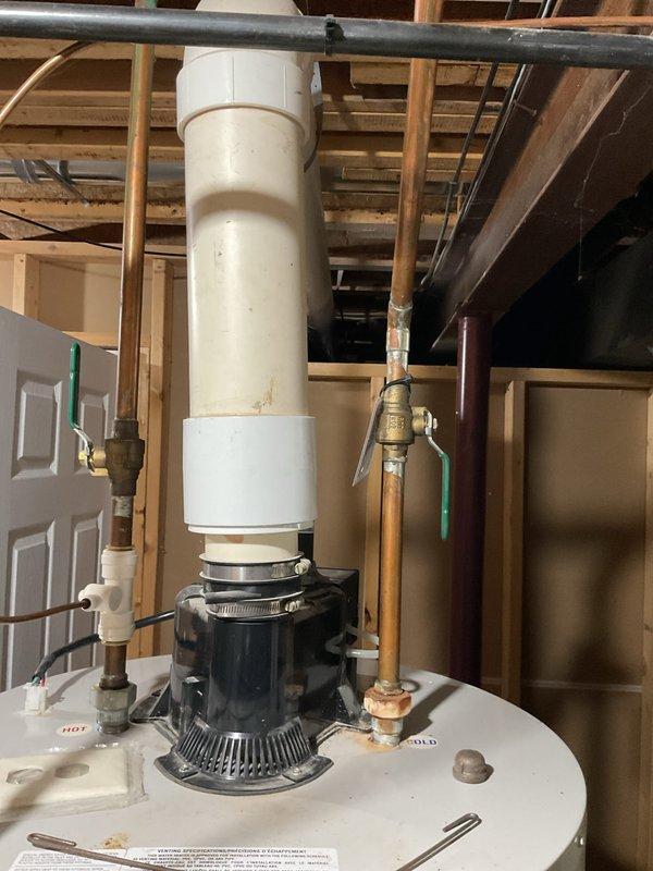 Completed comprehensive assessment of existing HVAC system and water heating equipment for replacement estimate. Evaluated current Bradford White water heater installation located in unfinished basement utility area, documenting existing configuration including power-vented exhaust system with black cylindrical draft inducer assembly mounted on top of unit. Inspected all plumbing connections including copper supply lines, brass shut-off valves, green-handled isolation valve, and flexible tubing connections. Assessed current PVC venting configuration running vertically through ceiling joists. Photographed existing installation showing water heater positioning beneath exposed floor framing, connection points, safety labels, and surrounding utility space constraints. Examined furnace system requiring replacement and documented spatial requirements for new equipment installation. Provided detailed replacement recommendations for both heating system and water heater upgrade, including equip