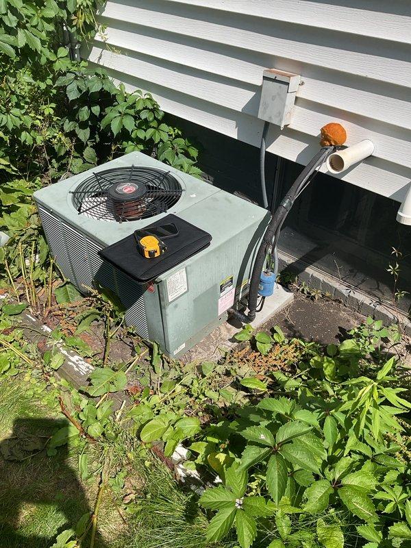 Conducted comprehensive assessment of existing HVAC system for air conditioning replacement. Evaluated current Evcon furnace unit in basement mechanical room, documenting condition of white PVC condensate drainage lines, refrigerant line connections with copper piping and red shut-off valves, and overall system configuration. Inspected outdoor condenser unit positioned against building exterior, noting vegetation encroachment around base and sides that will require clearance for new equipment installation. Photographed existing refrigerant line set with mixed insulation sections running along exterior wall to determine if lines can be reused or require replacement. Assessed electrical connections, condensate drainage routing, and accessibility for equipment removal and new system installation. Provided detailed estimate for complete air conditioning system replacement including outdoor condenser unit and associated components.