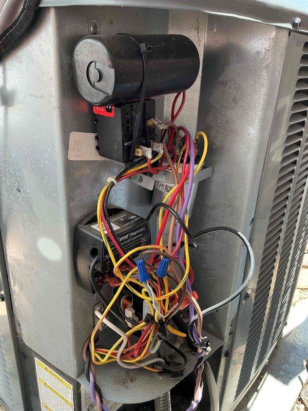 Completed preventive maintenance on 7-year-old residential air conditioning system. Removed access panel to inspect electrical components, tested capacitor and motor assembly functionality using diagnostic meter, verified proper wire connections and color-coded wiring integrity throughout the unit. Exterior condenser unit operating normally with adequate clearance from building structure and proper positioning on concrete pad.
