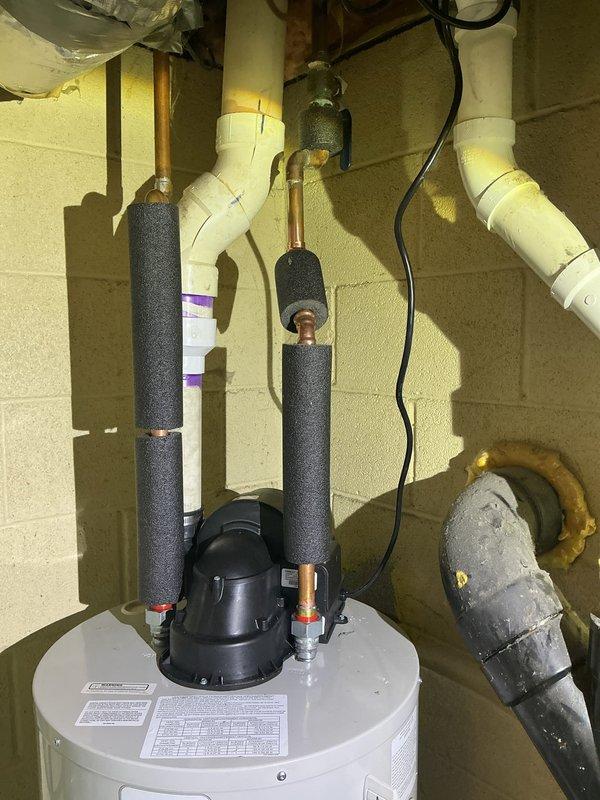 Responded to no hot water complaint at 48-year-old residence. Upon inspection, diagnosed failed tanked water heater requiring replacement. Removed old unit and installed new white cylindrical water heater in basement utility area. Connected copper supply lines with proper black foam pipe insulation to prevent heat loss and condensation. Installed recirculation pump with brass fittings at top of tank for improved hot water delivery throughout home. Verified all connections for leaks and proper operation. Used level to ensure tank installation meets manufacturer specifications for optimal performance and longevity. Tested system and confirmed hot water restoration to all fixtures.