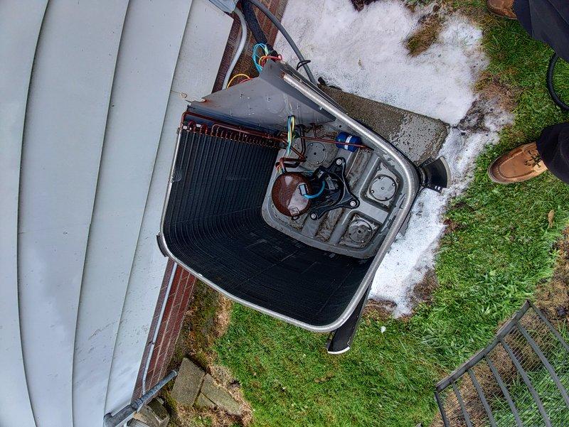Performed routine cooling maintenance on a 10-year-old residential air conditioning system. Removed access panel to inspect internal components including condenser coils, refrigerant lines, and electrical connections, confirming all systems were operating properly. Unit and surrounding area photographed for service documentation.