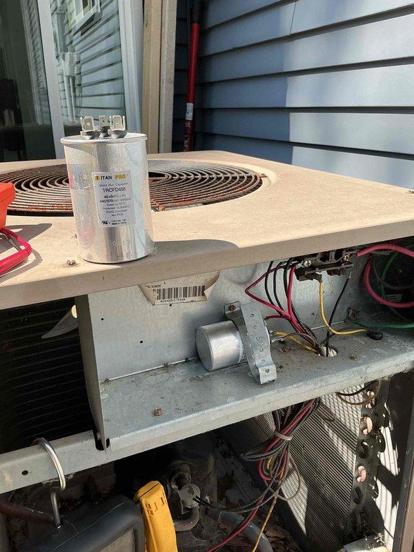 Responded to no cooling complaint on 26-year-old air conditioning system with both indoor and outdoor fans running but no cold air output and intermittent buzzing noise from outdoor unit. Upon inspection, diagnosed failed dual-run capacitor on outdoor condensing unit. Replaced defective TITAN PRO capacitor with properly rated replacement, restoring compressor operation. Verified system startup, confirmed proper amperage draw on compressor and condenser fan motor, and tested cooling performance. System now operating within normal parameters with cold air delivery restored throughout home.