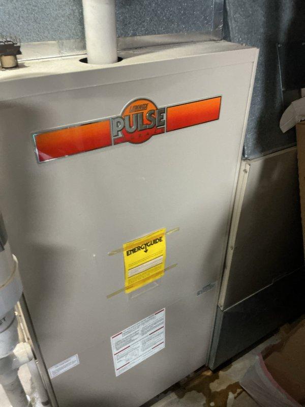 Responded to no cooling complaint on 47-year-old Lennox Pulse system with noise and drainage leak issues affecting entire home. Upon inspection, found unit had reached end of serviceable life with multiple component failures including compromised condensate drainage system causing water leakage at drain pipe. Documented existing equipment condition with photos showing aged furnace/HVAC unit in basement location with visible PVC venting and surrounding utility area. Advised customer that 1979-era Lennox Pulse system requires immediate replacement due to age, obsolete parts availability, and current system failures preventing proper operation and cooling capacity.