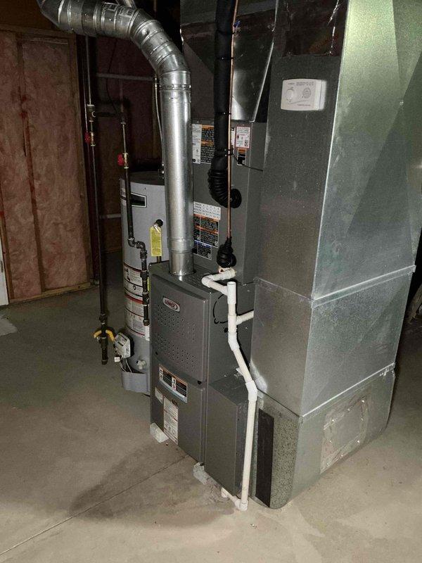 Responded to service call regarding newly installed AC units causing excessive noise during startup and dimming of household lights. Upon inspection, observed HVAC system installation in basement utility area with furnace and associated ductwork. Examined equipment components including motor assembly, electrical connections, and control systems. Documented current system configuration showing white PVC piping, metallic ductwork, and electrical wiring connections. Photographed equipment labels and specifications on units for reference. Issues indicate potential electrical concerns related to inrush current draw during compressor startup, which may require evaluation of dedicated circuit capacity and hard start kit installation to reduce startup amperage and minimize voltage drop affecting household lighting circuits.