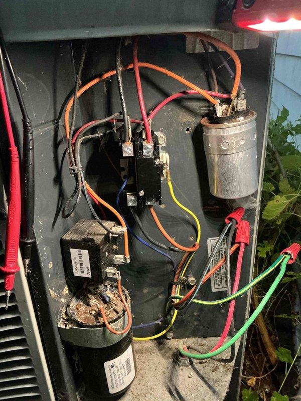 # Emergency No-Cool Service Call

Responded to emergency service call for non-operational air conditioning system on fifteen-year-old unit. Upon arrival, performed diagnostic evaluation of outdoor condensing unit with access panel removed to inspect electrical and mechanical components. Utilized test probes to measure voltage and verify electrical continuity across contactor, capacitor, and compressor terminals.

Inspection revealed aged electrical components including weathered dual-run capacitor showing signs of deterioration and accumulated debris throughout control compartment. Examined compressor windings, contactor operation, and all wire connections for proper voltage delivery and secure terminations. Multiple colored control wires (orange, red, yellow, blue, green) were inspected for integrity and proper routing between components.

Visual assessment documented condition of black compressor unit with manufacturer labeling intact, electrical relay/contactor assembly in center po