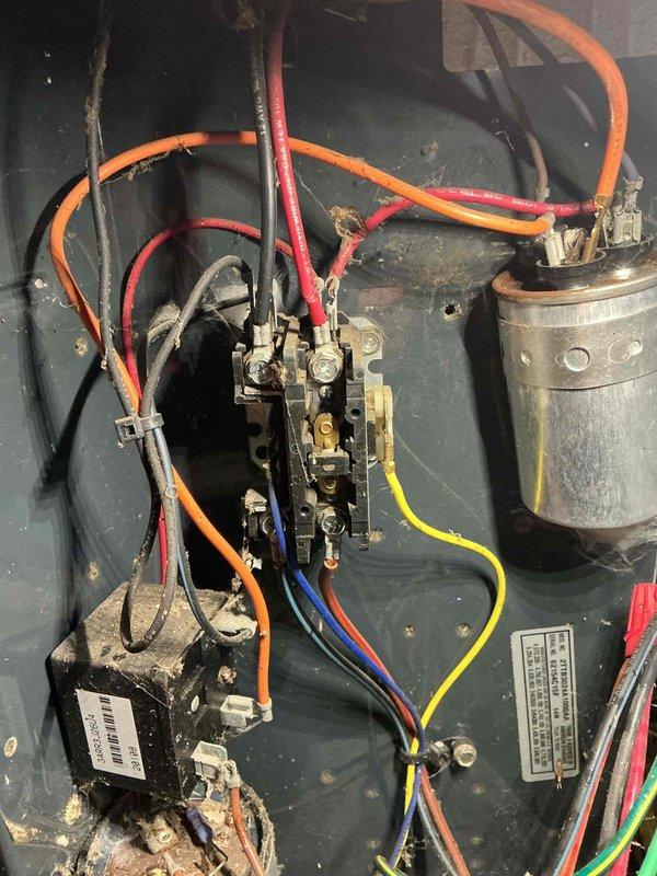 # Emergency No-Cool Service Call

Responded to emergency service call for non-operational air conditioning system on fifteen-year-old unit. Upon arrival, performed diagnostic evaluation of outdoor condensing unit with access panel removed to inspect electrical and mechanical components. Utilized test probes to measure voltage and verify electrical continuity across contactor, capacitor, and compressor terminals.

Inspection revealed aged electrical components including weathered dual-run capacitor showing signs of deterioration and accumulated debris throughout control compartment. Examined compressor windings, contactor operation, and all wire connections for proper voltage delivery and secure terminations. Multiple colored control wires (orange, red, yellow, blue, green) were inspected for integrity and proper routing between components.

Visual assessment documented condition of black compressor unit with manufacturer labeling intact, electrical relay/contactor assembly in center po