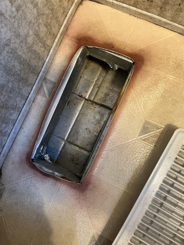 Responded to customer complaint of scorching smell from furnace register. Upon inspection, discovered significant heat damage and discoloration around floor register and ductwork, with visible staining and debris accumulation in the vent opening. Documented conditions with photographs showing brown discoloration pattern around metallic duct opening and compromised floor register, indicating potential airflow restriction or overheating issue requiring further system evaluation.