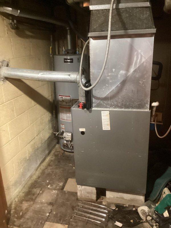 Conducted comprehensive assessment of existing HVAC system in residential basement utility area to provide replacement estimate for furnace and air conditioning equipment. Documented current installation configuration including furnace unit, ductwork connections, condensate drainage system, refrigerant line routing, and electrical conduit placement. Evaluated equipment accessibility, venting requirements, and spatial constraints for new system installation. Photographed existing setup showing furnace positioned against concrete block wall with associated PVC venting, copper refrigerant lines, and metal ductwork connections to facilitate accurate equipment sizing and replacement planning.