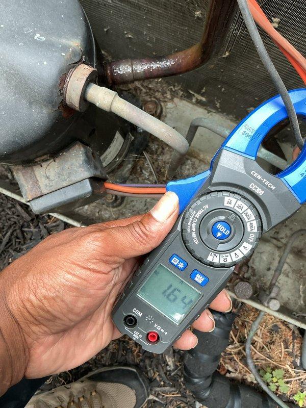 # HVAC Service Report

Responded to no cooling complaint affecting entire residence with 20-year-old air conditioning system. Upon arrival, performed diagnostic evaluation of outdoor condensing unit and electrical components.

Utilized digital clamp meter to measure electrical amperage on refrigerant lines, recording reading of 16.1 amps. Inspected compressor unit showing significant age-related wear, including surface corrosion on copper refrigerant lines and accumulated debris around equipment base. Outdoor unit positioned on concrete pad with visible deterioration and environmental exposure.

Opened and inspected electrical junction box revealing multiple wire connections with signs of aging. Observed terminal block component #6216 with various colored wire connections including yellow, purple, orange, black, and brown conductors. Noted visible corrosion, debris accumulation, and organic material within electrical enclosure, indicating prolonged exposure to outdoor elements. Termina