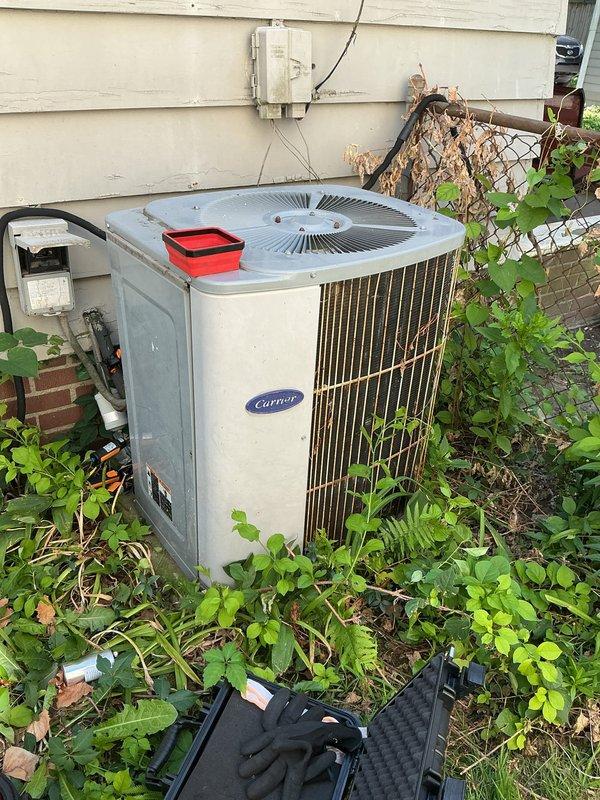 Responded to service call for 15-year-old Carrier air conditioning system not operating properly. Upon arrival, found outdoor condensing unit heavily overgrown with vegetation restricting airflow to condenser coils and impeding proper heat exchange. Cleared weeds, plants, and debris from around unit perimeter to restore adequate clearance for ventilation. Inspected condenser coil fins for damage and blockage caused by plant material. Removed accumulated dirt and organic matter from top grille and fan assembly. Verified electrical disconnect and wiring connections were secure and free from vegetation interference. System tested and confirmed operational following clearance of obstructions and restoration of proper airflow around unit.