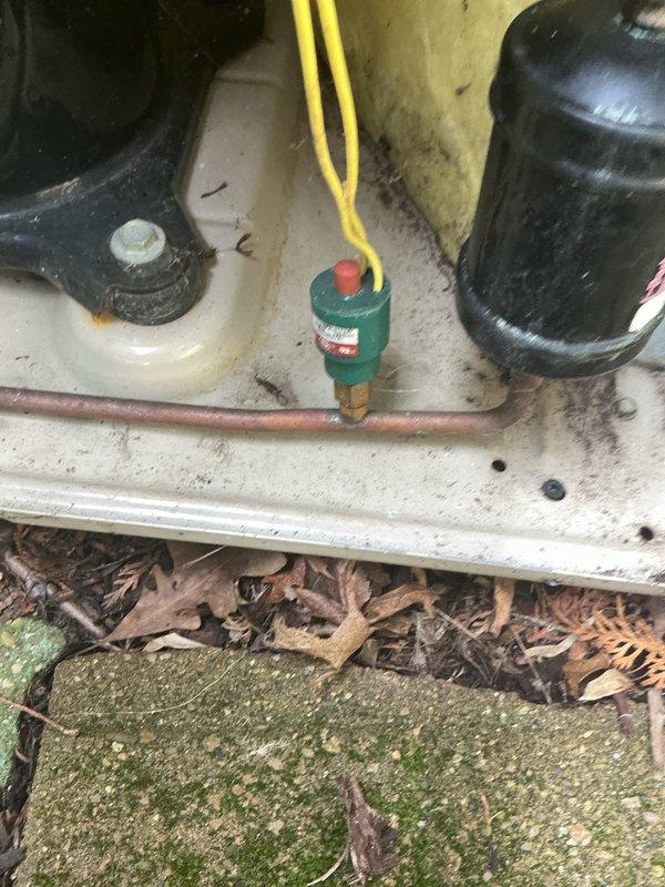 # HVAC Service Report

Responded to no cooling complaint on 22-year-old residential air conditioning system. Upon arrival, confirmed unit was not operating and producing no cool air. Visual inspection revealed compressor and outdoor unit components showed significant age-related wear and environmental deterioration.

Performed electrical diagnostics using clamp meter to measure amperage draw on compressor circuit. Readings indicated minimal current flow at 0.12 amps, well below normal operating parameters for compressor operation. Inspected high-pressure safety switch mounted on refrigerant lines, which appeared to be in tripped position based on visual assessment of reset button.

Examined copper refrigerant line connections and found evidence of outdoor unit exposure to moisture and debris accumulation on concrete pad. Dead leaves and organic material had collected around base of unit, and moss growth was present on surrounding surfaces, indicating prolonged exposure to damp conditio