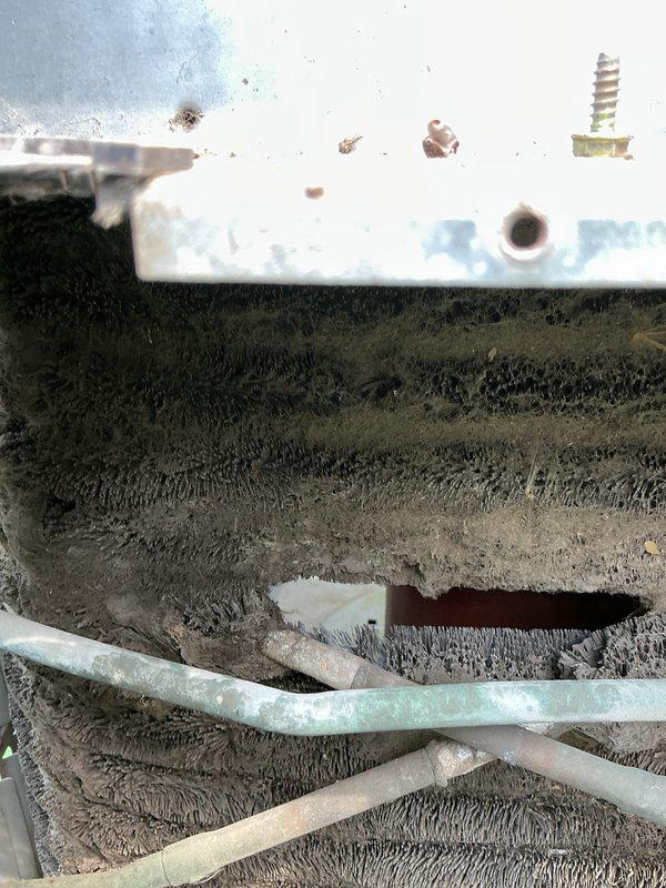 # HVAC Tune-Up Service Completed

Performed comprehensive tune-up service on a 32-year-old air conditioning system. Upon inspection, discovered severe accumulation of dust, dirt, and fibrous debris coating the evaporator coils and interior components, indicating extended period without maintenance. The buildup was several inches thick in areas, significantly restricting airflow and reducing system efficiency. 

Documented existing conditions through photography showing the heavily contaminated evaporator coil assembly with matted, fibrous material obscuring metal surfaces. White painted interior surfaces displayed minor rust spots and corrosion. Drainage components including light blue condensate lines were visible beneath the debris layer.

Exterior inspection revealed standard residential installation with white electrical disconnect box mounted on light green vinyl siding, connected via flexible metal conduit to electrical service above. Gray utility access panel with visible copper