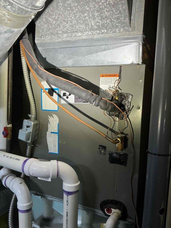 Documented existing HVAC system installation for replacement estimate purposes. The current setup includes a gray metal furnace unit with associated condensate drainage system, electrical connections, and refrigerant lines. Photographed all components including PVC drain piping with proper trap configuration, flexible electrical conduit, and existing cabinet assembly to provide comprehensive documentation for preparing replacement equipment quote and identifying any modifications needed for new system installation.