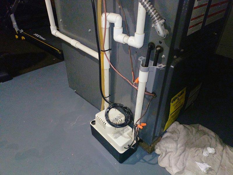 Responded to service call for water accumulation under furnace in basement. Upon inspection, identified condensate drainage issue originating from upper section of condensate line assembly. Examined condensate pump system, PVC drain line configuration with P-trap, and associated connections to furnace air handler unit. Traced source of water leak to compromised connection point at top portion of condensate hose where it interfaces with primary drain line. Verified condensate pump operation and cleared any blockages in drainage system. Secured all connections, tested system operation under normal condensing conditions, and confirmed proper drainage flow with no further leakage detected.