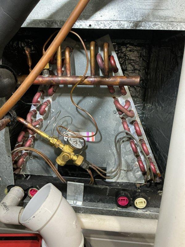 Completed routine maintenance tune-up on 10-year-old residential air conditioning system. Upon inspection, discovered significant frost and ice accumulation on evaporator coils and metal surfaces within the air handler unit, indicating restricted airflow or potential refrigerant issues. Documented internal components including copper refrigerant lines, evaporator coil assembly, condensate drain line, and service valves for maintenance records.